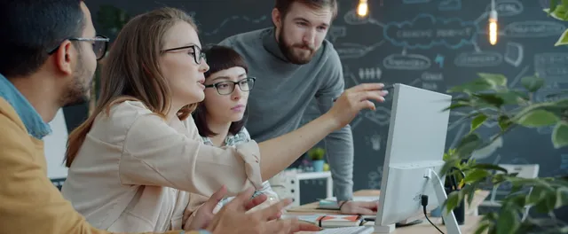 A team of engineers gathered around a monitor in an office, discussing their work.