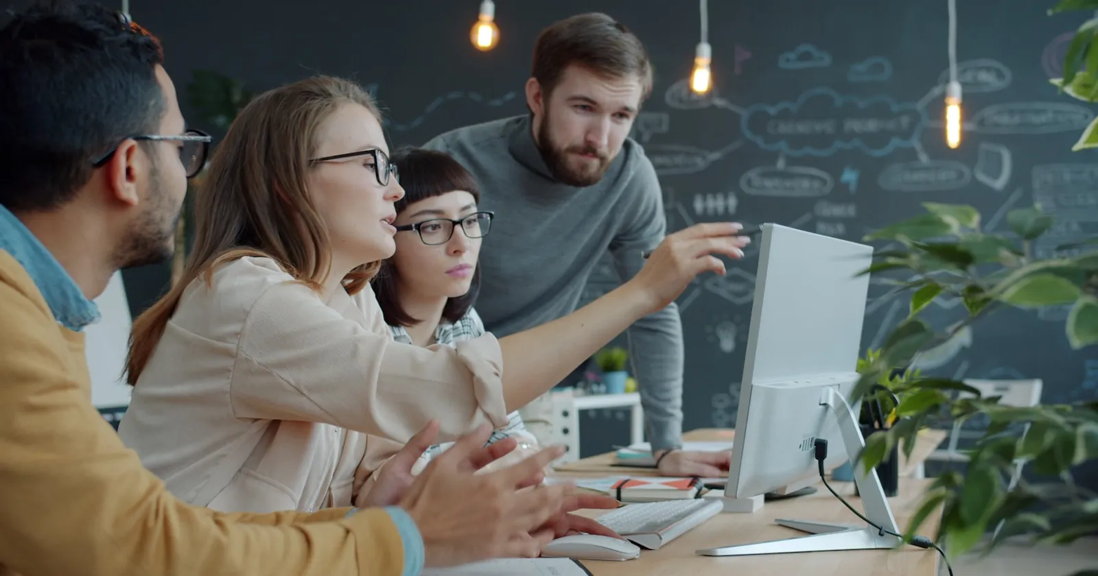 A team of engineers gathered around a monitor in an office, discussing their work.