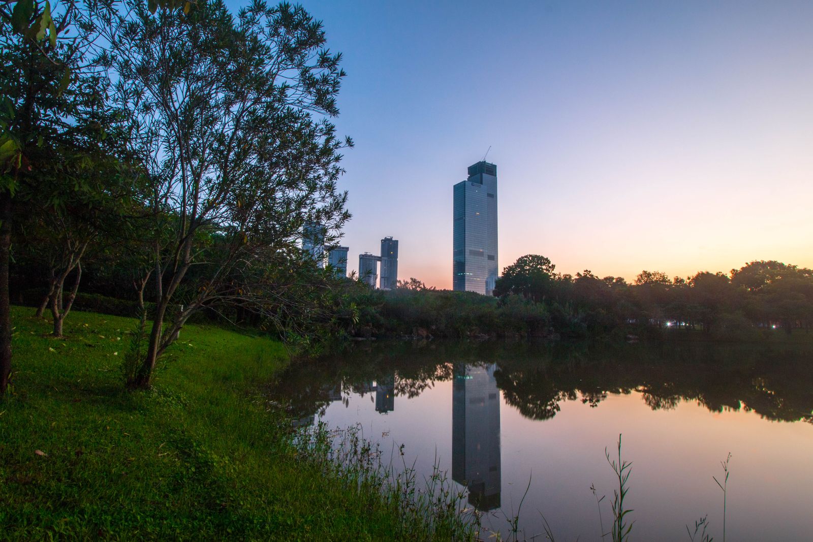 Skyscraper reflected in a park lake at dusk, China