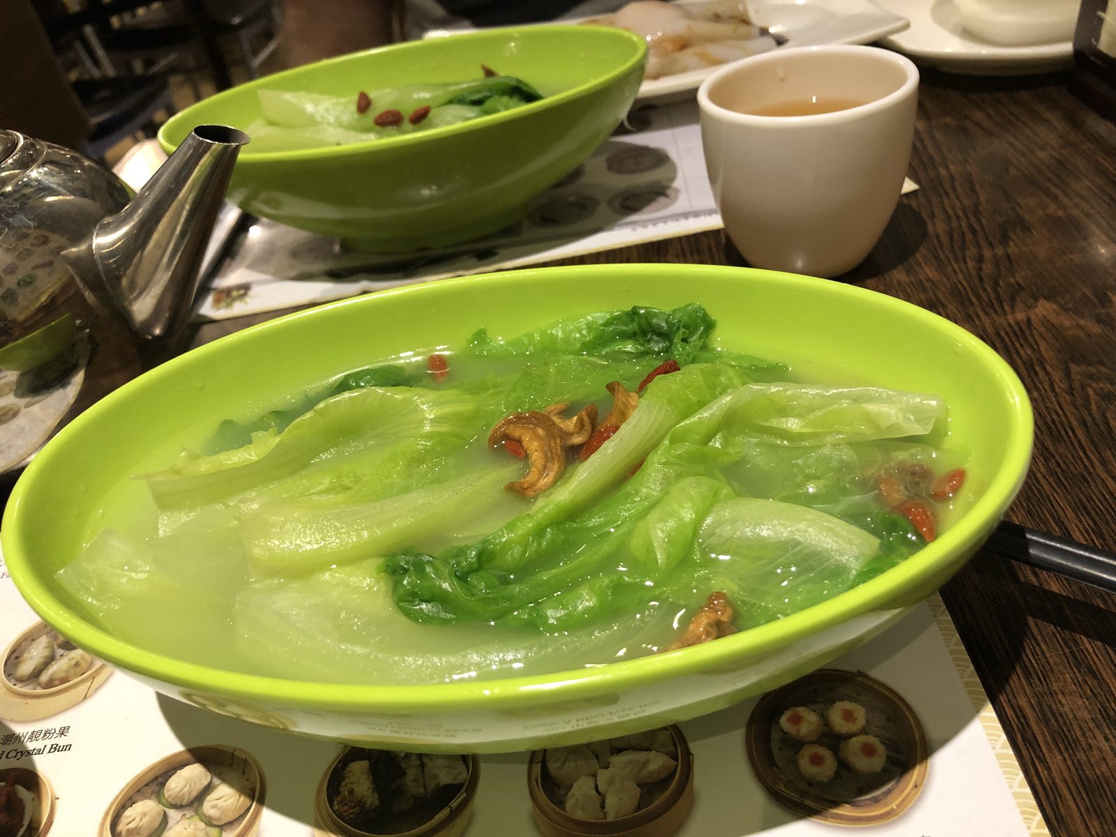Bright green poached lettuce in broth on a dim sum table